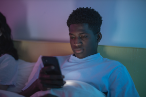 Young male sitting in bed on phone